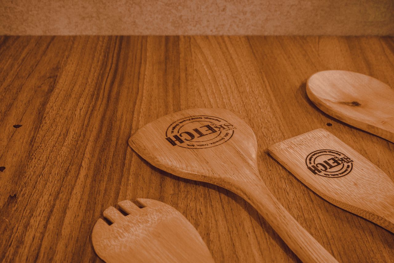 Vue rapprochée d’ustensiles de cuisine en bois posés sur une surface rustique en bois, idéale pour des thématiques culinaires.